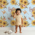 Lovely child standing in front of Whimsy Tots Sun-Kissed Meadow Blooms in Sky with sunflower, flower, leaf, bouquet in design.