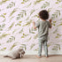 Lovely child standing in front of Whimsy Tots Botanical Breeze Wallpaper in Blush Pink with leaf, sprig, branch, stem in design.