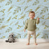 Lovely child standing in front of Whimsy Tots Botanical Breeze Wallpaper in Sky with leaf, sprig, branch, stem in design.