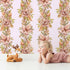 Lovely child standing in front of Whimsy Tots Vintage Garden Climb Wallpaper in Blush Pink with flower, vine, leaf, bouquet in design.
