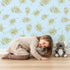 Lovely child standing in front of Whimsy Tots Gentle Palm Scatter Wallpaper in Blue with leaf, palm in design.