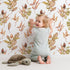 Lovely child standing in front of Whimsy Tots Autumn Forage Garden Wallpaper in White with leaf, pod, sprig, branch in design.