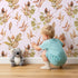Lovely child standing in front of Whimsy Tots Autumn Forage Garden Wallpaper in Blush Pink with leaf, pod, sprig, branch in design.