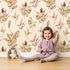 Lovely child standing in front of Whimsy Tots Autumn Forage Garden Wallpaper in Taupe Beige with leaf, pod, sprig, branch in design.