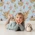 Lovely child standing in front of Whimsy Tots Autumn Forage Garden Wallpaper in Sky with leaf, pod, sprig, branch in design.