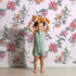 Lovely child standing in front of Whimsy Tots Winter Blooming Garden Wallpaper in Blush Pink with flower, cotton, eucalyptus, poinsettia in design.