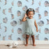 Lovely child standing in front of Whimsy Tots Celestial Winter Blooms Wallpaper in Sky with moon, flower, cotton, eucalyptus in design.