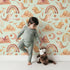 Lovely child standing in front of Whimsy Tots Whimsical Earth Friends Wallpaper in Mint Green with whale, dolphin, narwhal, bird, fish, rainbow, moon, mountain, cloud in design.