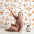 Lovely child standing in front of Whimsy Tots Golden Star Scatter Wallpaper in White with star in design.