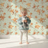 Lovely child standing in front of Whimsy Tots Golden Star Scatter Wallpaper in Mint with star in design.