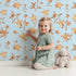 Lovely child standing in front of Whimsy Tots Golden Star Scatter Wallpaper in Sky Blue with star in design.