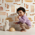 Lovely child standing in front of Whimsy Tots Painted Rhythm Wallpaper in White with line, brushstroke in design.