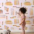Lovely child standing in front of Whimsy Tots Painted Rhythm Wallpaper in Blush Pink with line, brushstroke in design.