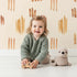 Lovely child standing in front of Whimsy Tots Painted Simplicity Wallpaper in Cream with line, brushstroke in design.