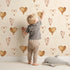 Lovely child standing in front of Whimsy Tots Heartfelt Balloons Wallpaper in Cream with heart, balloon, outline in design.