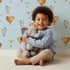 Lovely child standing in front of Whimsy Tots Heartfelt Balloons Wallpaper in Sky with heart, balloon, outline in design.