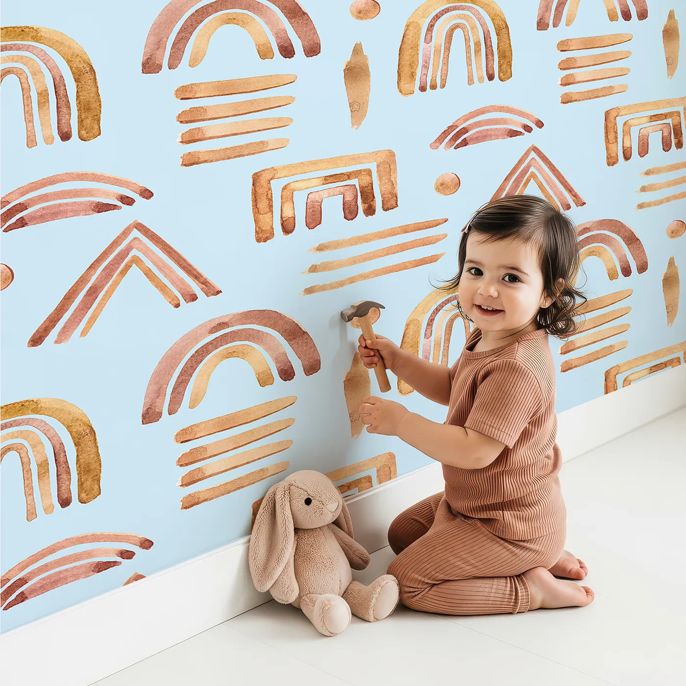 Lovely child standing in front of Whimsy Tots Sun-Drenched Shapes Wallpaper in Sky with rainbow, shape, brushstroke, line, dot in design.