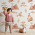 Lovely child standing in front of Whimsy Tots Feathered Serenity Wallpaper in White with bird, swan, crown, mountain, wing in design.