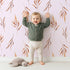 Lovely child standing in front of Whimsy Tots Rustle and Grace Wallpaper in Blush Pink with branch, leaf, stem, botanical in design.