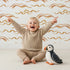 Lovely child standing in front of Whimsy Tots Soft Wave Rhythm Wallpaper in White with wave, curve, line, brushstroke, abstract in design.