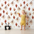 Lovely child standing in front of Whimsy Tots Terracotta Diamond Dance Wallpaper in White with diamond, shape, rust, abstract, terracotta in design.
