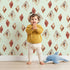 Lovely child standing in front of Whimsy Tots Terracotta Diamond Dance Wallpaper in Mint Green with diamond, shape, rust, abstract, terracotta in design.