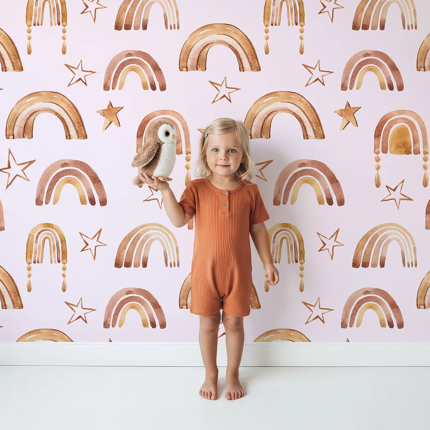 Lovely child standing in front of Whimsy Tots Golden Boho Rainbows Wallpaper in Blush with rainbow, star in design.