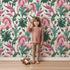 Lovely child standing in front of Whimsy Tots Enchanted Meadow Prance Wallpaper in Mint Green with unicorn, flower, tulip, leaf in design.