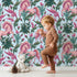 Lovely child standing in front of Whimsy Tots Enchanted Meadow Prance Wallpaper in Blue with unicorn, flower, tulip, leaf in design.