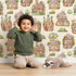 Lovely child standing in front of Whimsy Tots Secret Garden Cutaway Homes Wallpaper in Sand with house, root, tree, mushroom, gourd in design.