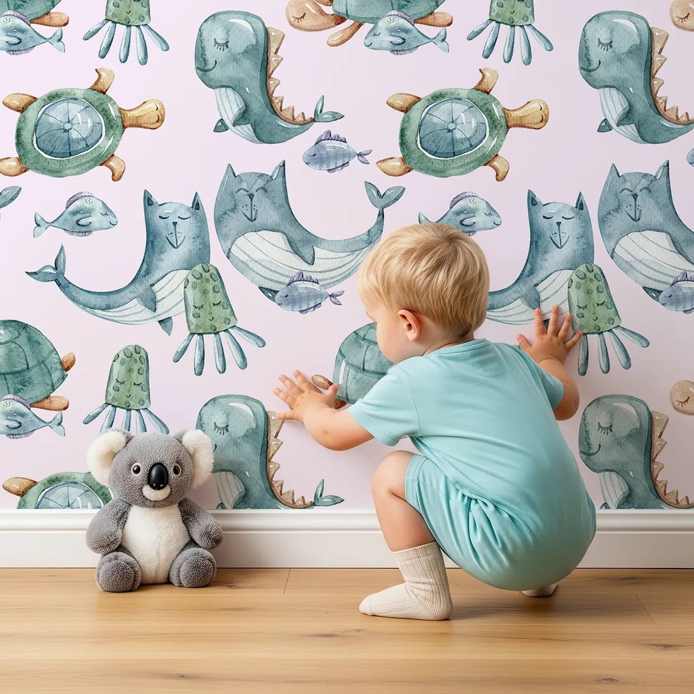 Lovely child standing in front of Whimsy Tots Ocean Pals Parade Wallpaper in Blush Pink with whale, turtle, fish, octopus, jellyfish, sea dragon in design.