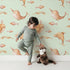 Lovely child standing in front of Whimsy Tots Blushing Ocean Friends Wallpaper in Mint Green with whale, dolphin, narwhal, fish, wave in design.