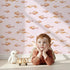 Lovely child standing in front of Whimsy Tots Sleepy Blush Fish Wallpaper in Pink with fish, wave in design.