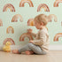 Lovely child standing in front of Whimsy Tots Boho Brush Rainbow Wallpaper in Mint Green with rainbow, stripe, arch in design.