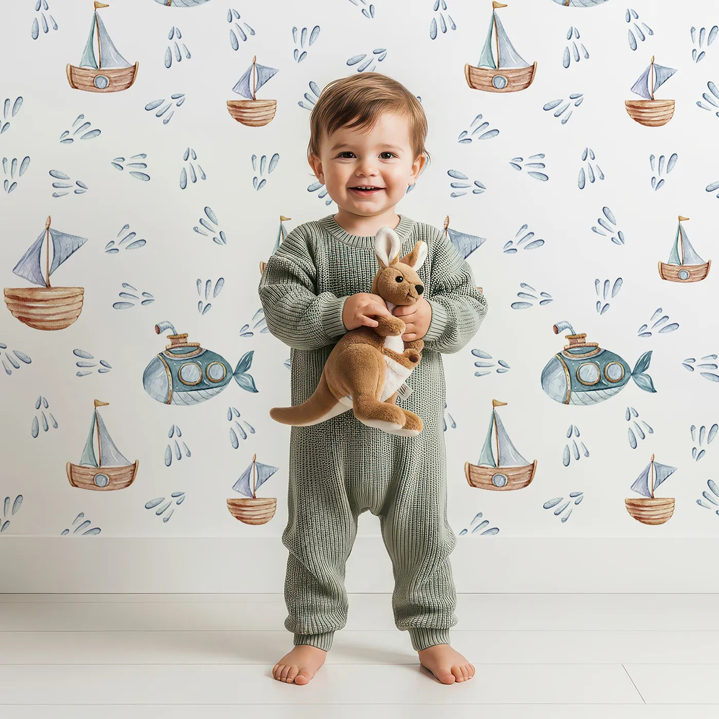 Lovely child standing in front of Whimsy Tots Seaside Vessel Parade Wallpaper in White with boat, submarine, splash, sail in design.