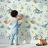 Lovely child standing in front of Whimsy Tots Deep Sea Discovery Wallpaper in Mint Green with whale, fish, submarine, jellyfish, seaweed, boat in design.