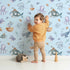 Lovely child standing in front of Whimsy Tots Deep Sea Discovery Wallpaper in Blue with whale, fish, submarine, jellyfish, seaweed, boat in design.