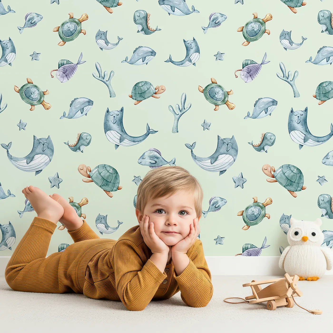 Lovely child standing in front of Whimsy Tots Dreamy Sea Pals Wallpaper in Mint Green with whale, turtle, fish, star, coral in design.