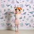 Lovely child standing in front of Whimsy Tots Whale Song Friends Wallpaper in Pink with whale, fish, narwhal, octopus, jellyfish in design.