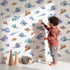 Lovely child standing in front of Whimsy Tots Sleepy Fish Friends Wallpaper in White with fish, fin, ocean, bubble in design.