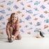 Lovely child standing in front of Whimsy Tots Sleepy Fish Friends Wallpaper in Blush Pink with fish, fin, ocean, bubble in design.
