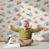 Lovely child standing in front of Whimsy Tots Sleepy Fish Friends Wallpaper in Sand with fish, fin, ocean, bubble in design.