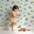 Lovely child standing in front of Whimsy Tots Sleepy Fish Friends Wallpaper in Mint Green with fish, fin, ocean, bubble in design.