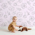 Lovely child standing in front of Whimsy Tots Petal Outline Bloom Wallpaper in Blush Pink with flower, petal, bell flower, sprig, leaf, botanical in design.