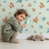 Lovely child standing in front of Whimsy Tots Starlight Scribbles Wallpaper in Green with star, scribble, doodle in design.