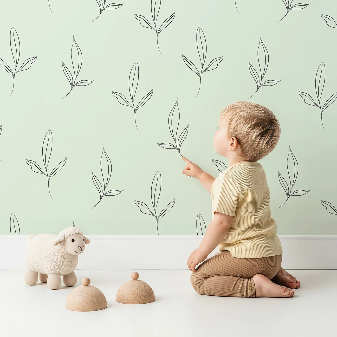 Lovely child standing in front of Whimsy Tots Whispering Leaflines Wallpaper in Mint Green with leaf, sprig, botanical, line art in design.