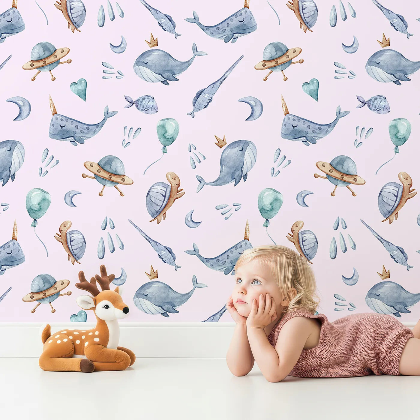 Lovely child standing in front of Whimsy Tots Galactic Ocean Friends Wallpaper in Blush Pink with whale, turtle, narwhal, balloon, moon, UFO, droplet, crown in design.