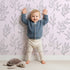 Lovely child standing in front of Whimsy Tots Wild Leafline Garden Wallpaper in Blush Pink with leaf, botanical, sprig, berry, line art in design.