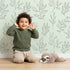 Lovely child standing in front of Whimsy Tots Wild Leafline Garden Wallpaper in Mint Green with leaf, botanical, sprig, berry, line art in design.
