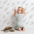Lovely child standing in front of Whimsy Tots Leaf Outline Symphony Wallpaper in White with leaf, branch, botanical, outline in design.